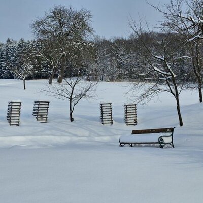 The winter landscape of the farmhouse with snow-covered fields, trees, and a bench.