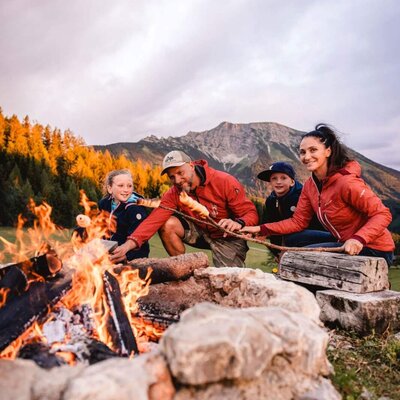 Guests enjoy an outdoor campfire and roast food, surrounded by mountain scenery at the farmhouse.