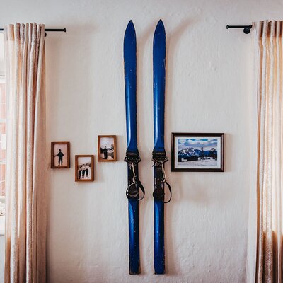 Interior decor in the farmhouse, featuring vintage blue skis, framed photos, and two windows with light curtains.
