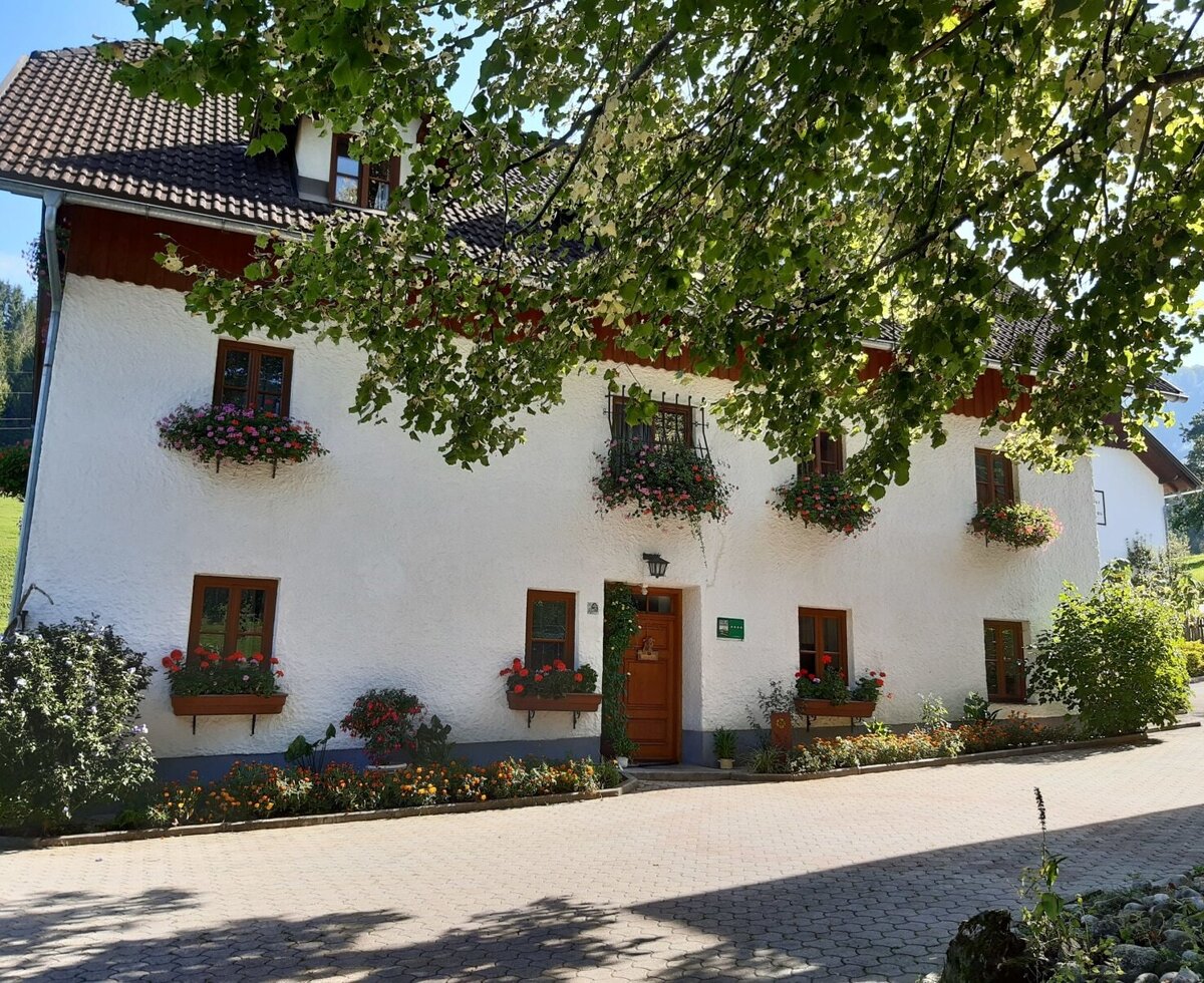 The farm house exterior with white walls, brown-framed windows adorned with colorful flower boxes, and a paved entrance area.