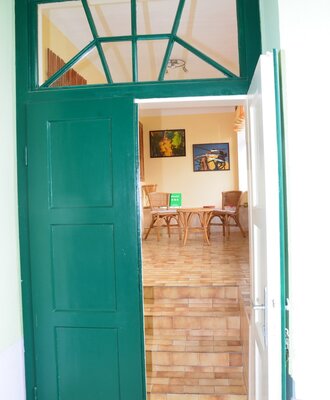 Green entrance door of the holiday apartment in the farmhouse, opening into a living space with tiled floor and wicker seating.