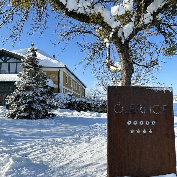 The snow-covered exterior of the ÖLERHOF farm house, featuring its five-star sign.