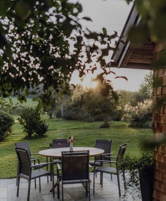An inviting stone terrace at the farmhouse's chalet, featuring comfortable outdoor seating in the idyllic orchard bathed in evening light.