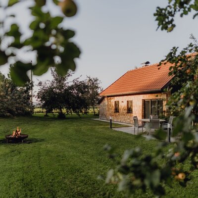 The farmhouse's inviting chalet set in a lush orchard, featuring a cozy outdoor fire pit and a seating area.