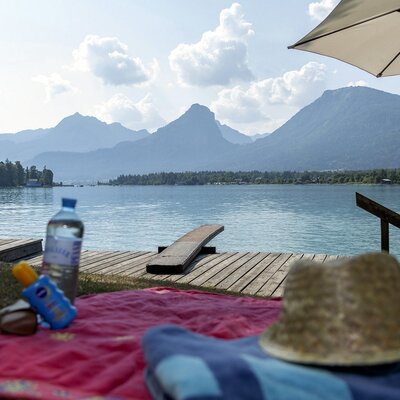 The farmhouse provides a lakeside area on Lake Wolfgangsee with a wooden pier, sun umbrella, and panoramic mountain views.