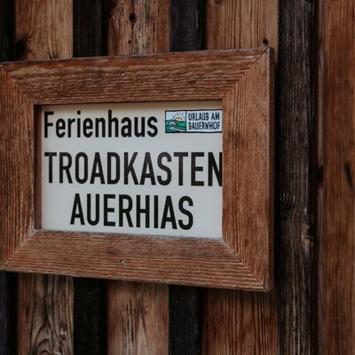 The wooden sign at the Farm House, displaying "Ferienhaus Troadkasten Auerhias" and the "Urlaub am Bauernhof" logo.