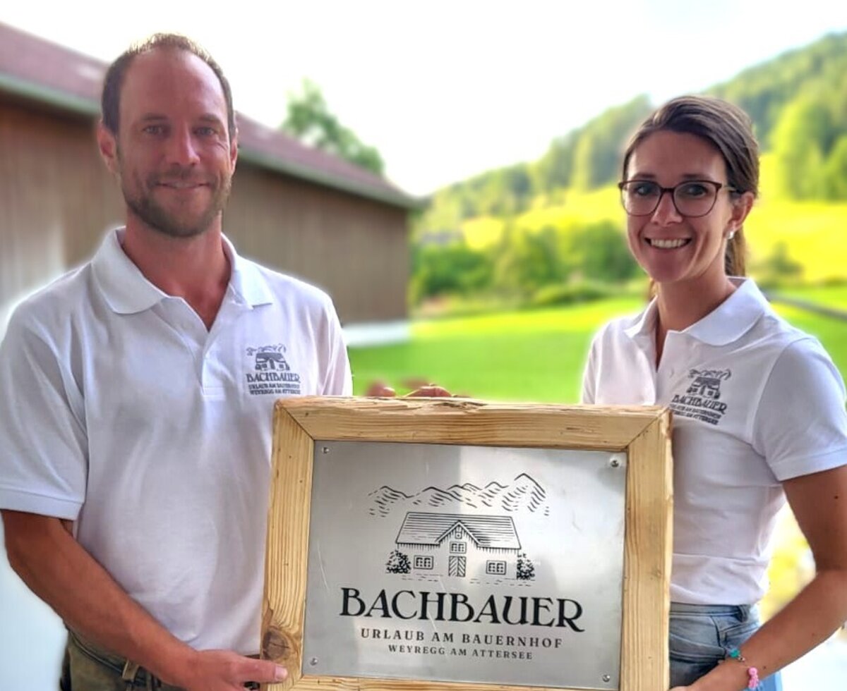 The hosts of the Bachbauer farm house, holding a sign that indicates holidays on the farm.