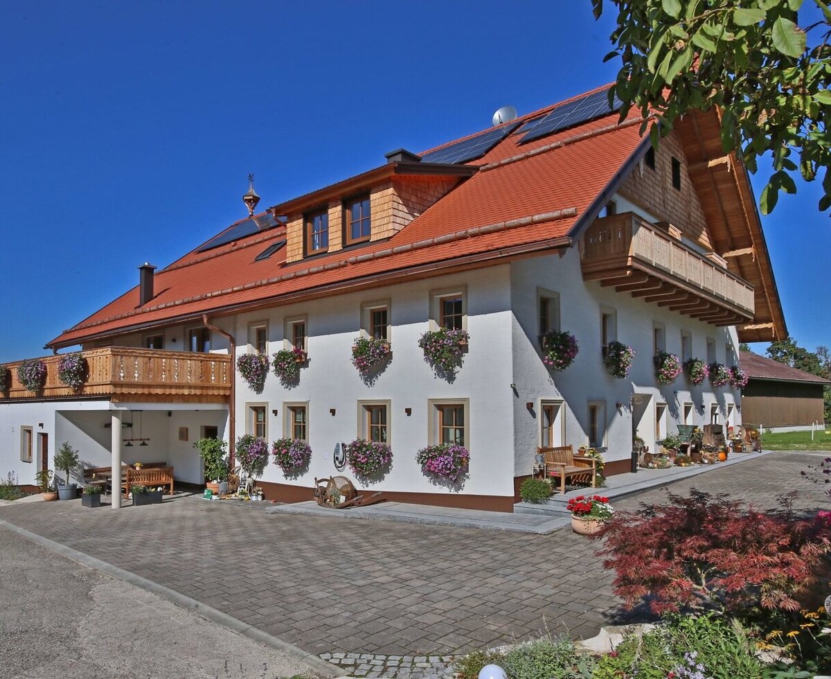 Exterior view of the farmhouse with white walls, wooden balconies, flower boxes, and a paved driveway.