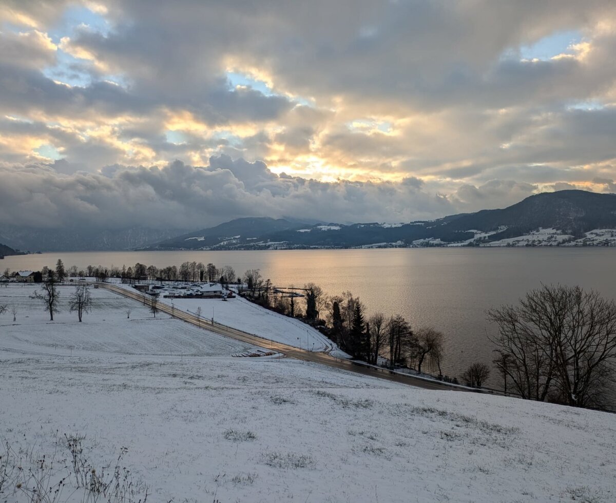 View from the farmhouse of Lake Attersee and the snow-covered winter landscape with mountains at sunset.