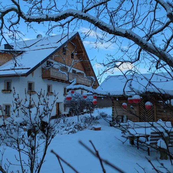 The snow-covered farmhouse in winter, featuring traditional wooden architecture, balconies, and red decorations.