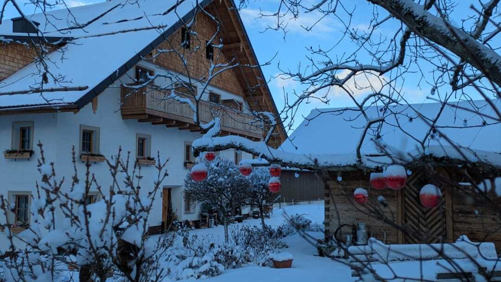 The snow-covered farmhouse in winter, featuring traditional wooden architecture, balconies, and red decorations.