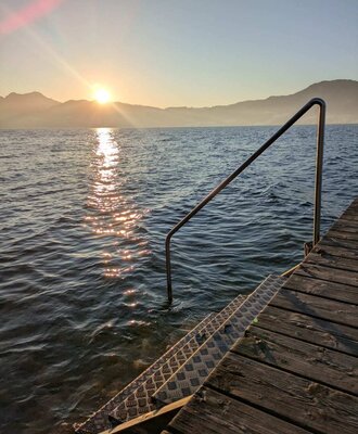 The farmhouse's private swimming area on Lake Attersee, featuring a jetty and steps for water access at sunset.