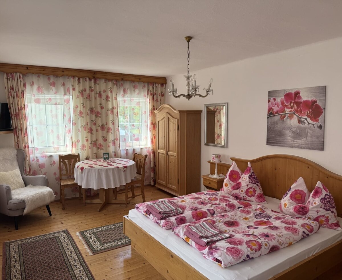 Double room in the farmhouse with a wooden bed, wardrobe, table, two chairs, and two windows.