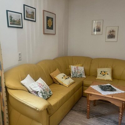 Living area of the farmhouse with a yellow corner sofa, coffee table, and pictures on the wall.