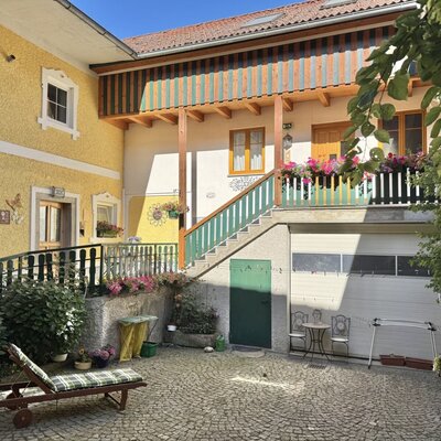 Exterior view of the farmhouse with a paved courtyard, sun lounger, and the bike garage.