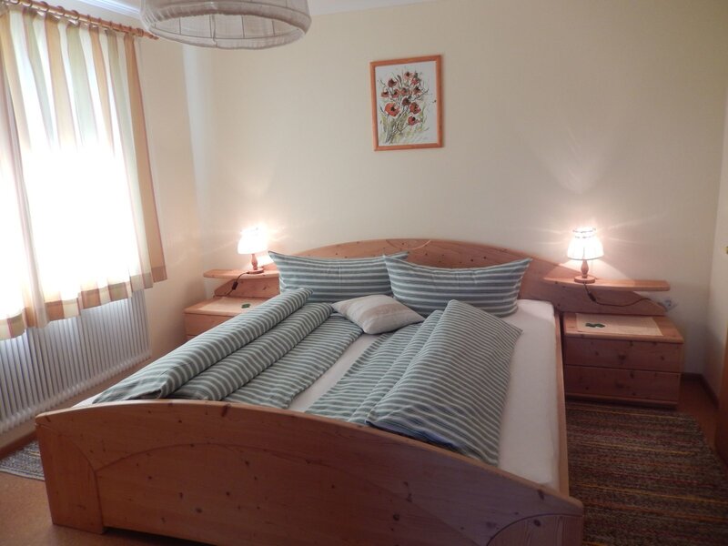 Double bedroom in the farmhouse featuring a wooden bed, striped duvets, two bedside tables with lamps, and a window with curtains.