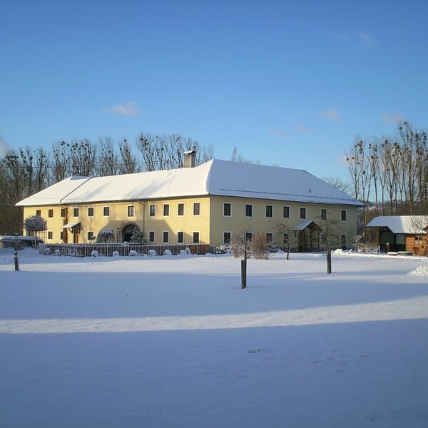 The light yellow Farm House with its roof and surrounding grounds covered in snow during winter.