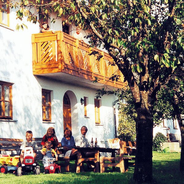 The farm house exterior features a wooden balcony, a garden with outdoor seating, and toy cars for children.