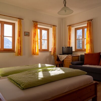 Guest room in the Farm House offering two single beds, a sofa bed, a television, and windows with mountain views.