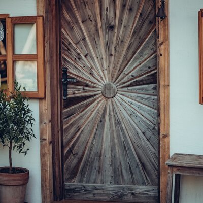 The main entrance of the farmhouse features a wooden door with a sunburst design, traditional wooden-framed windows with lace curtains, and potted lemon trees.