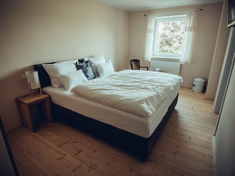 Farmhouse bedroom with a double bed, wooden floor, a bedside table with a lamp, and a window.
