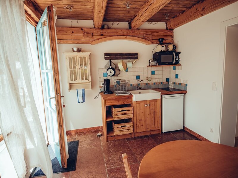 Kitchenette in the farm house featuring a sink, mini-fridge, microwave, and a dining table, with exposed wooden ceiling beams and an exit to the outside.