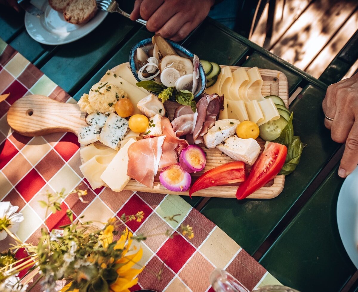 A wooden board displaying a selection of cheeses, cured meats, pickled vegetables, and fresh peppers on a table at the farmhouse.