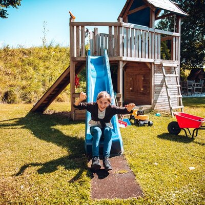 The farm house features an outdoor playground with a wooden structure and a blue slide for children.