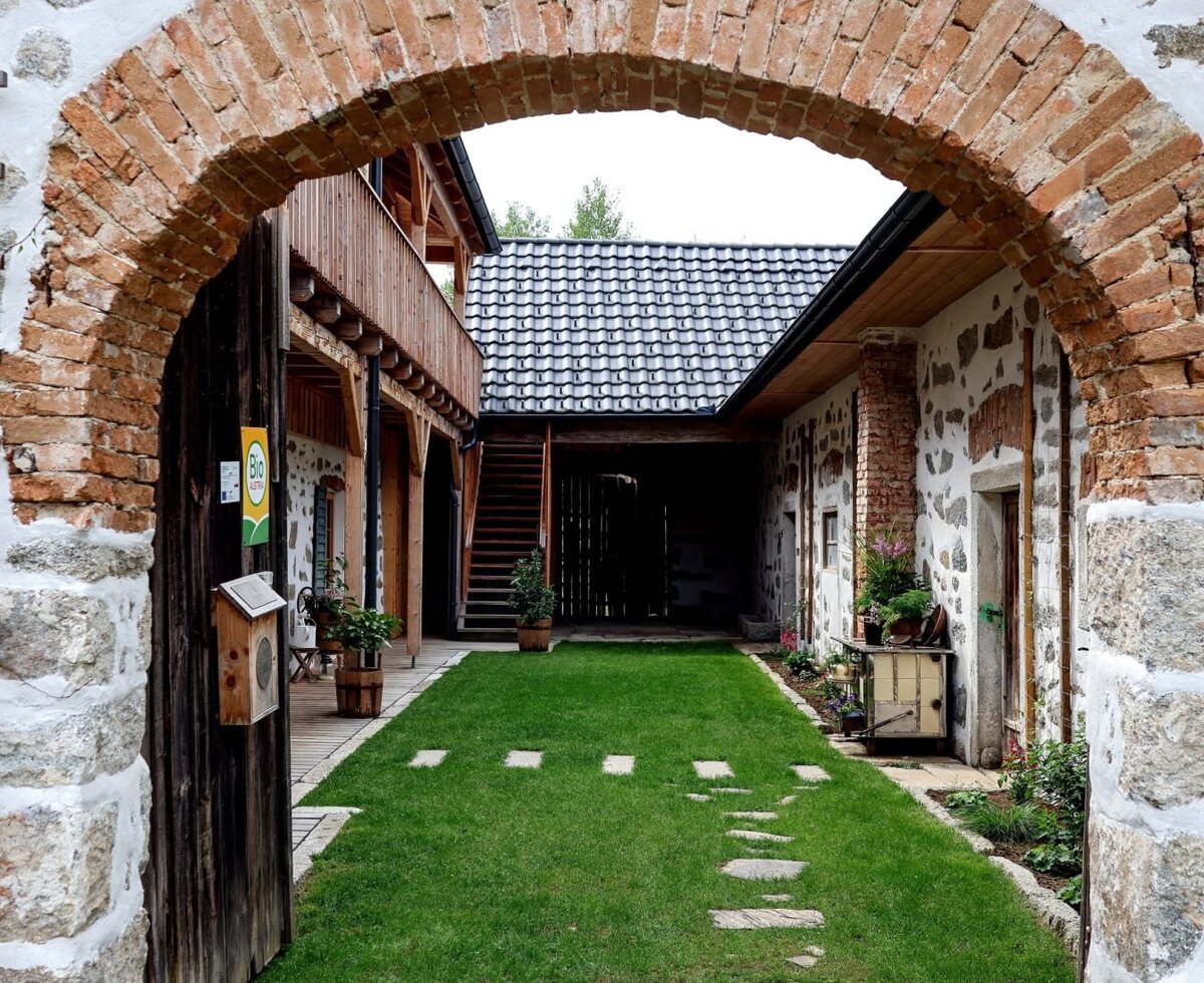 The farmhouse's inviting courtyard featuring a manicured lawn, a historic brick archway, and charming stone walls.