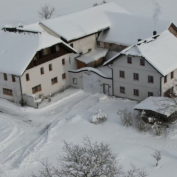 The snow-covered farmhouse exterior featuring multiple buildings and tracks in the snowy ground.