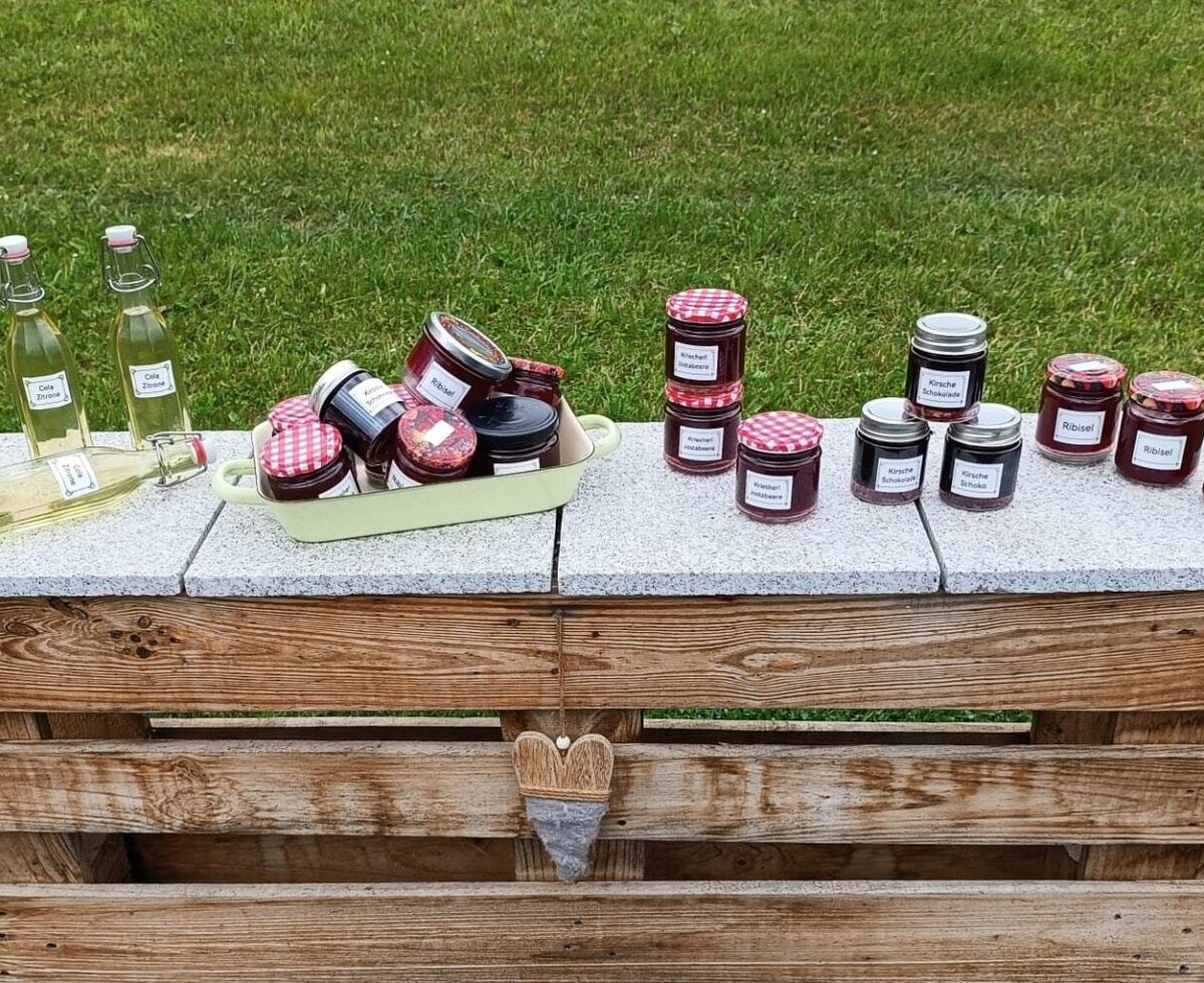 Homemade products from the Bauernhof, including various jams and drinks, displayed on a wooden stand.