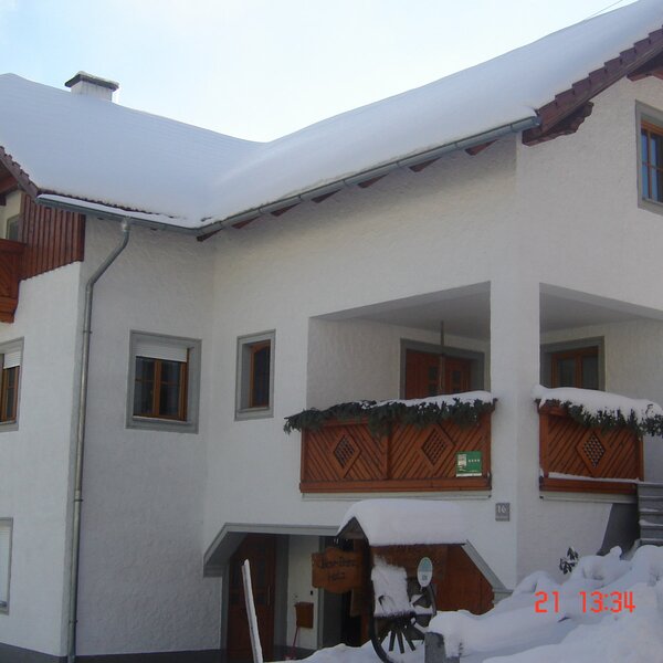 The Farm House exterior, featuring snow on the roof and grounds, traditional wooden balconies, and a covered entrance.