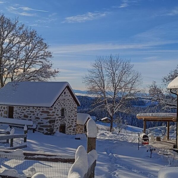 The rebuilt farmhouse and the historic 15th-century stone building are covered in snow, surrounded by a winter landscape.