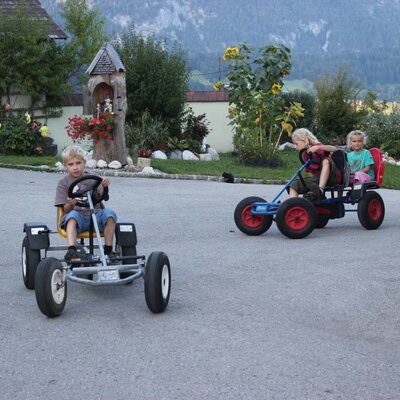 Children riding pedal go-karts on the grounds of the farmhouse.