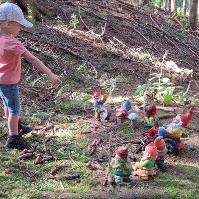 A child points at a group of garden gnomes in the forest surroundings of the farmhouse.