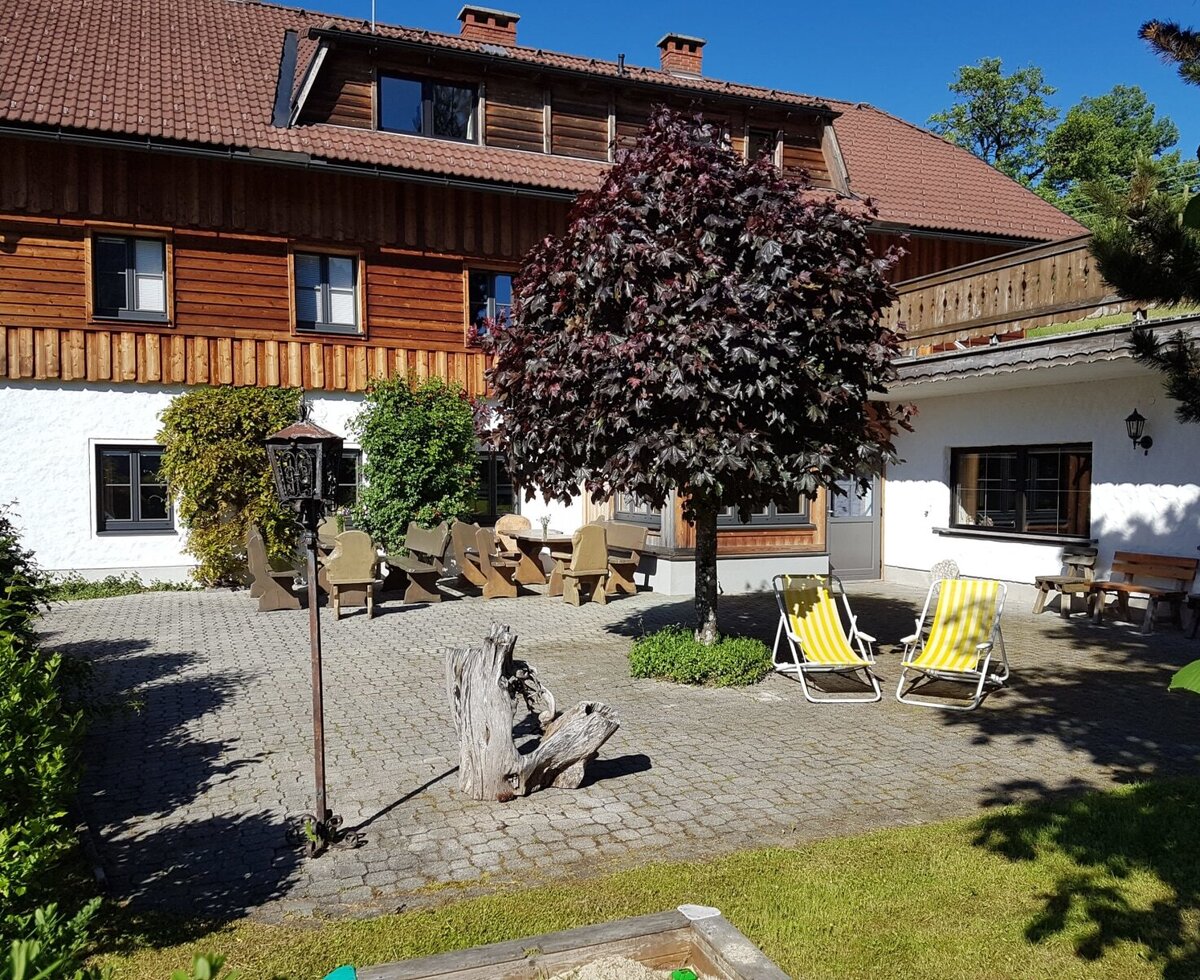 The exterior of the Farm House, featuring a paved terrace with wooden tables, benches, and sun loungers.
