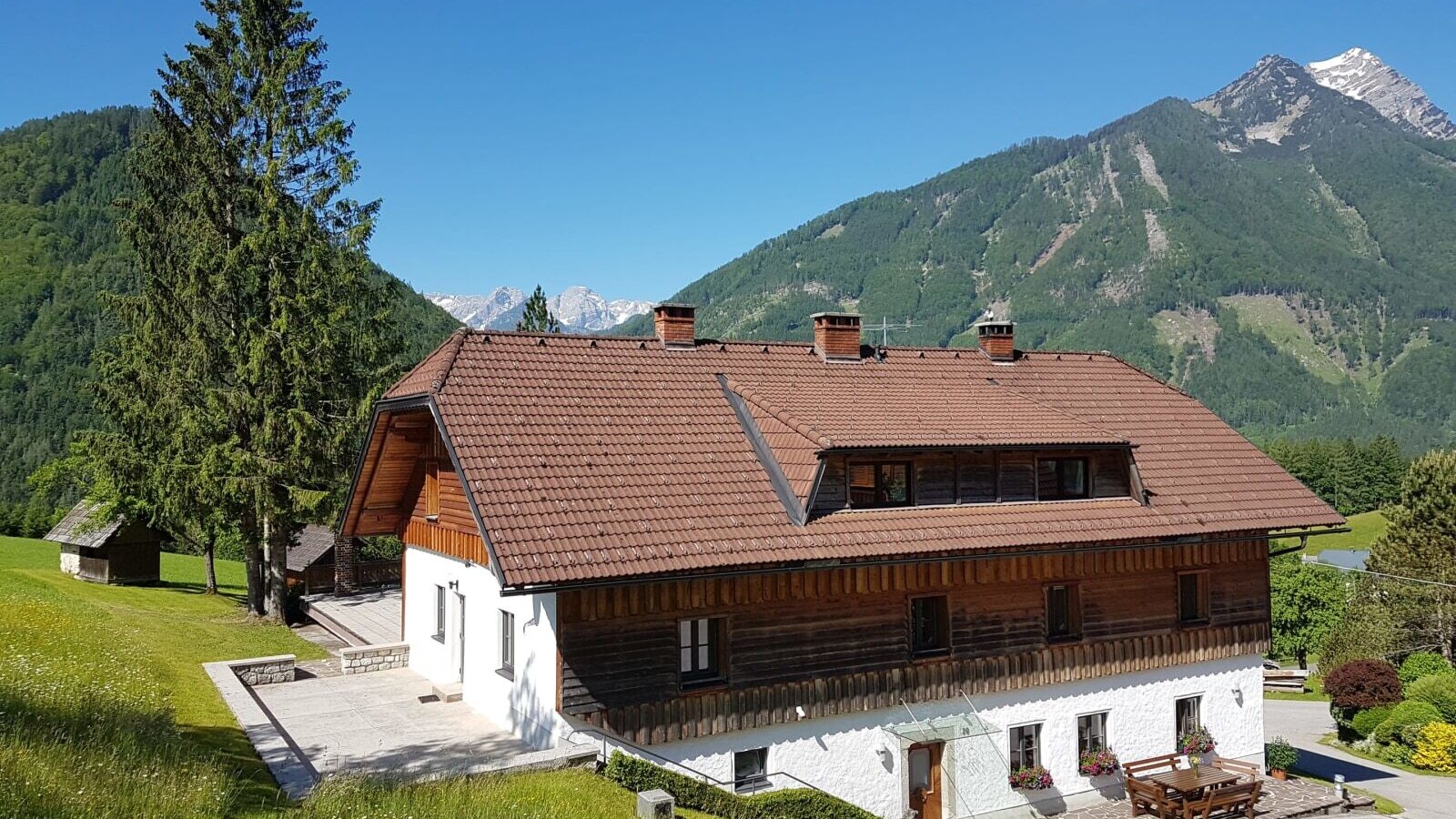 The Farm House, featuring a white and wooden exterior, outdoor terraces with a picnic table, and surrounding mountain views.