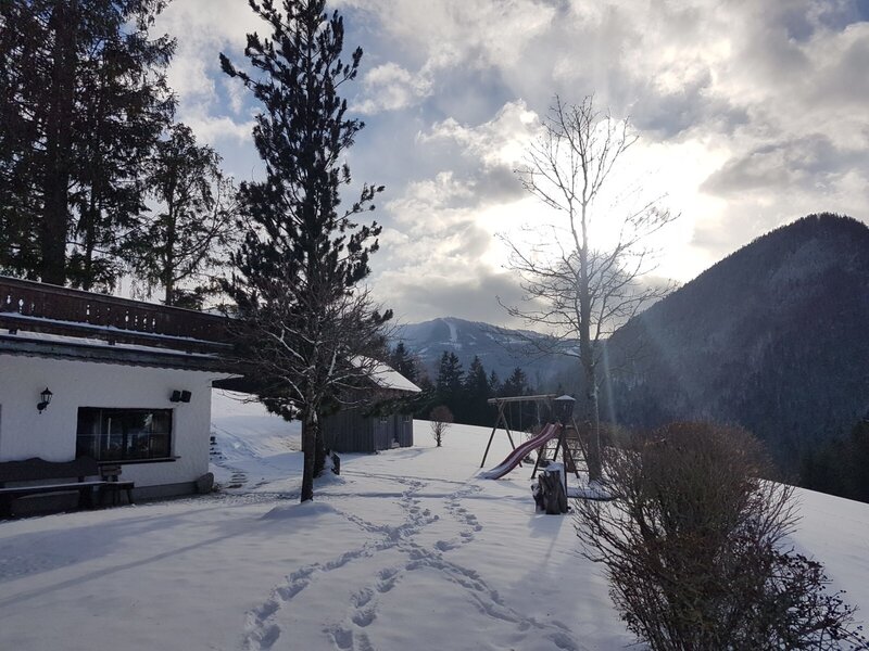 The Farm House exterior in winter, featuring the outdoor play area with a swing set and slide, and mountain views.