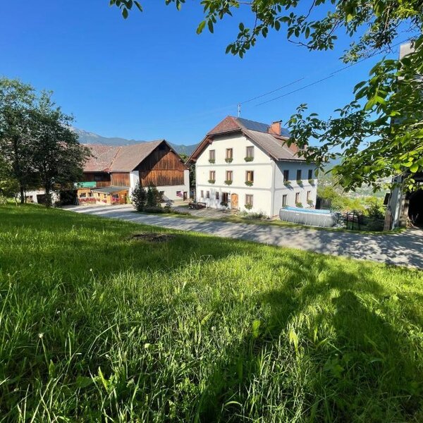 The farmhouse featuring a white main building, adjacent barns, a grassy area, and an above-ground pool.