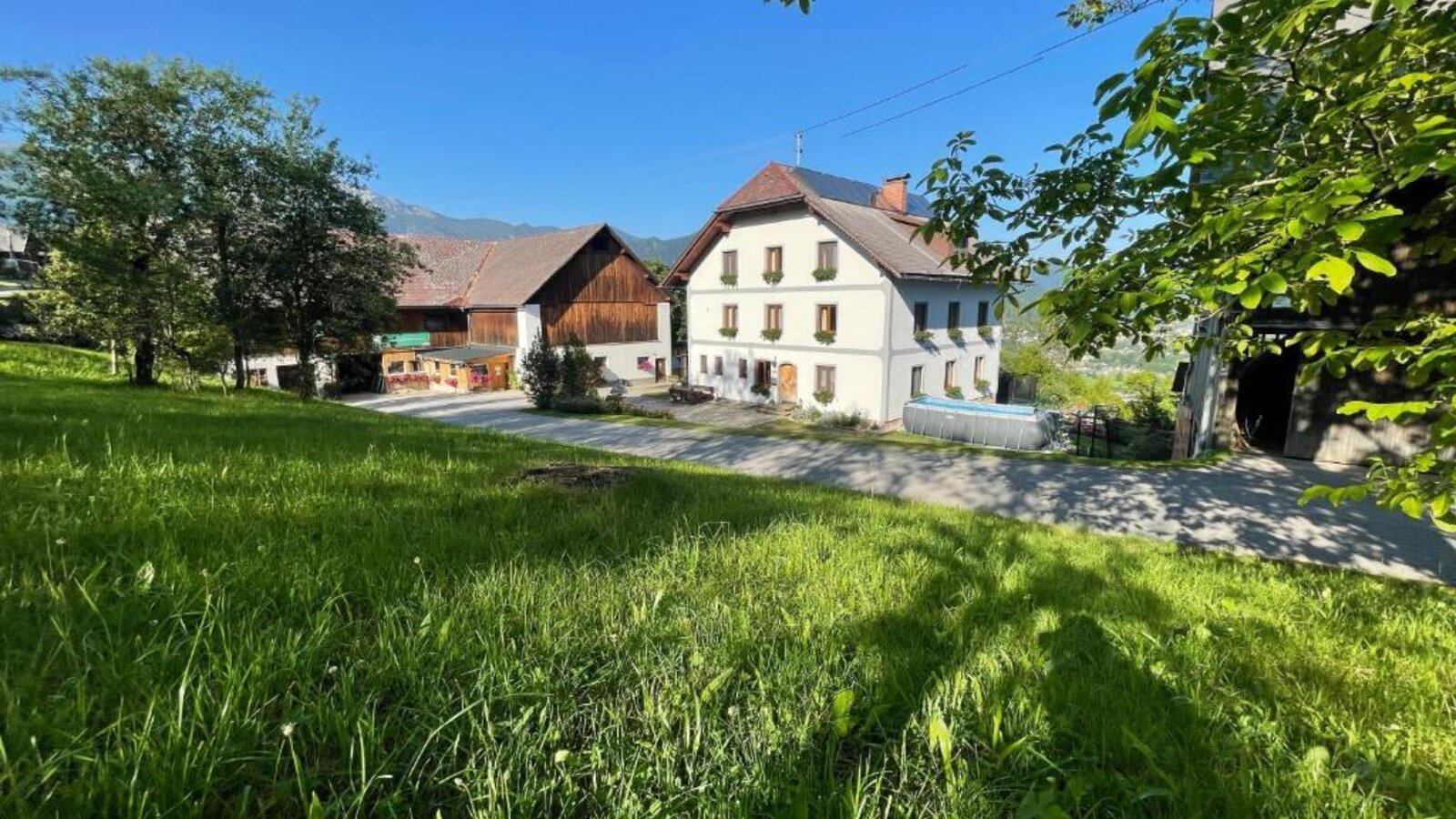 The farmhouse featuring a white main building, adjacent barns, a grassy area, and an above-ground pool.