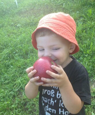 A child with a fresh red apple from the farmhouse.