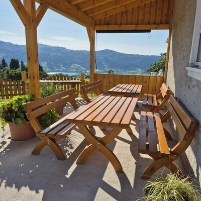 Covered balcony of the farmhouse with a wooden table and benches, offering a view of the lake and mountains.