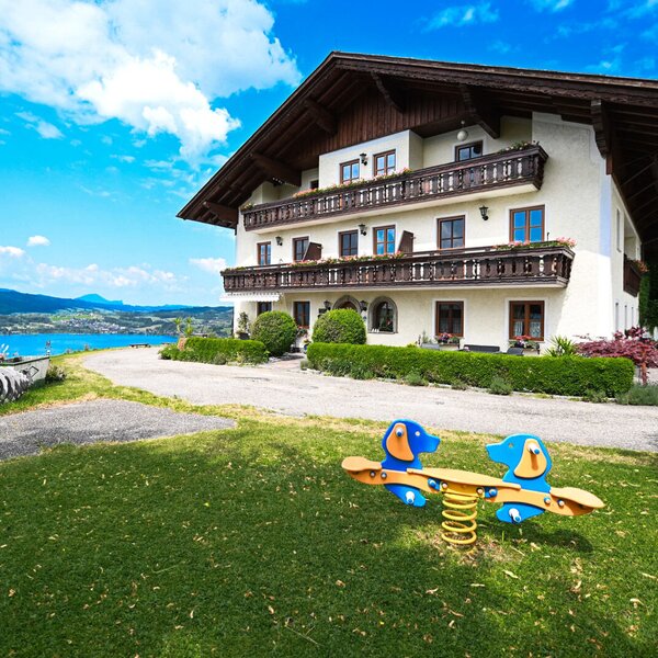 The farm house exterior features balconies, a children's spring rider on the lawn, and views of the lake and mountains.