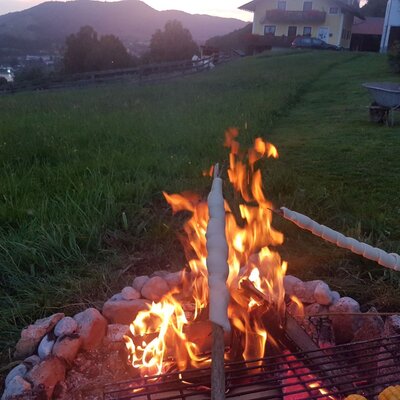 An outdoor campfire at the Farm House, featuring stick bread and corn being cooked over the fire, with mountain views in the distance.