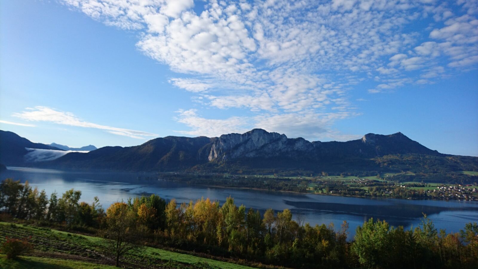 View of the lake and mountains from the Farm House, with green fields and trees in the foreground.