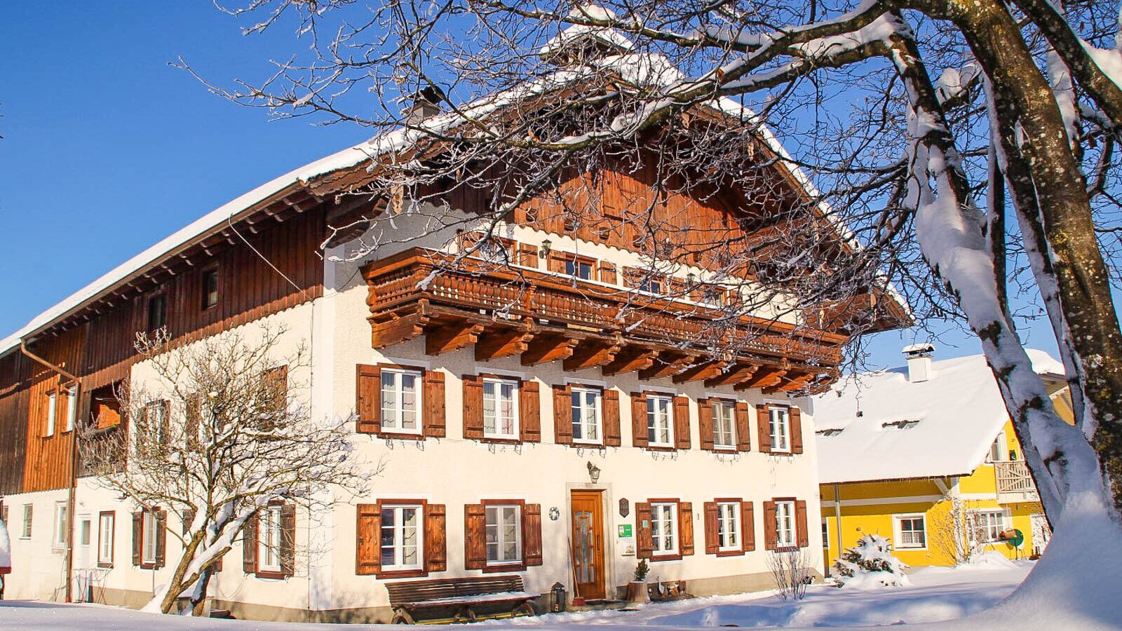 The farm house exterior, surrounded by snow, features traditional wooden balconies and window shutters.