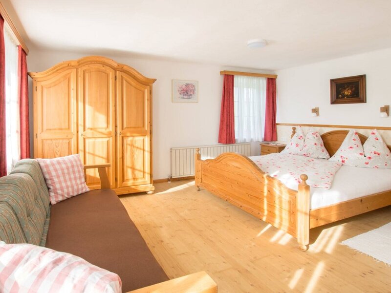 Bedroom in the farm house featuring a wooden double bed, two nightstands, a wardrobe, a sofa, and windows with red curtains.