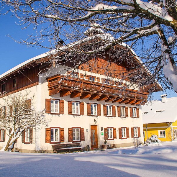 The farm house exterior, surrounded by snow, features traditional wooden balconies and window shutters. The farm house exterior, surrounded by snow, features traditional wooden balconies and window shutters.