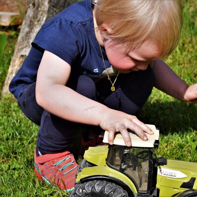 A child playing with a toy tractor on the grassy area of the farm house.
