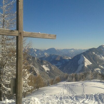The snowy mountain landscape near the Farm House, featuring ski tracks and a wooden summit cross.
